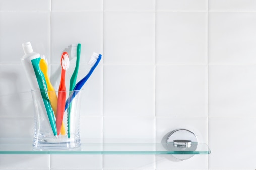 Des brosses à dents et un tube de dentifrice dans une tasse en verre sur l'étagère de la salle de bain