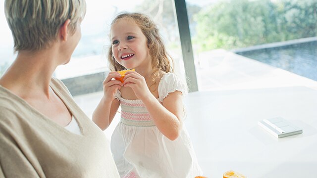 Fille regardant sa mère pendant qu'elle mange un fruit
