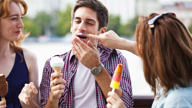 Trois personnes avec des glaces; l’une étale de la crème glacée sur la joue d’une personne qui rit.