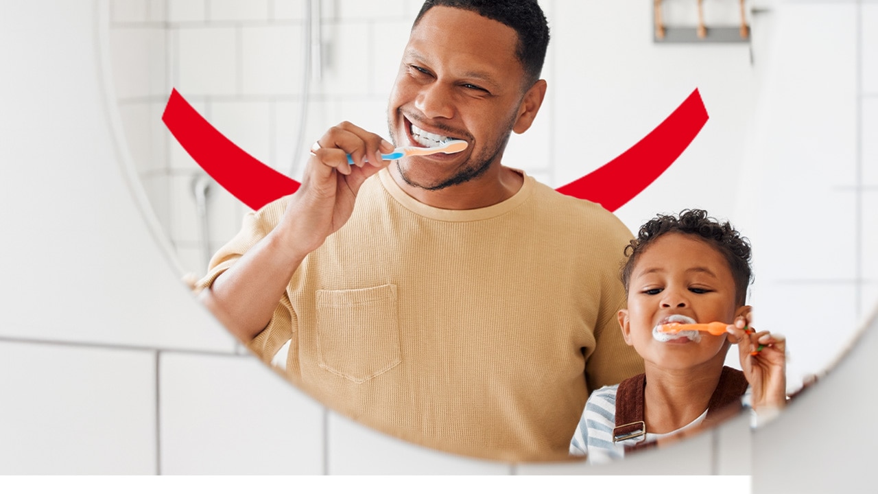 Un homme et un jeune enfant se brossant les dents joyeusement devant un miroir, avec le texte « Dentifrice au fluor : 7 points essentiels à connaître »