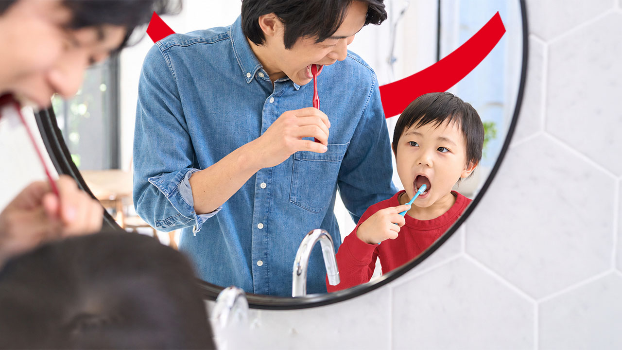 Un père et son jeune enfant se brossant les dents ensemble devant un miroir, avec la superposition de texte « Dentifrice pour enfants - Recommandations pédiatriques concernant l'utilisation du dentifrice ».