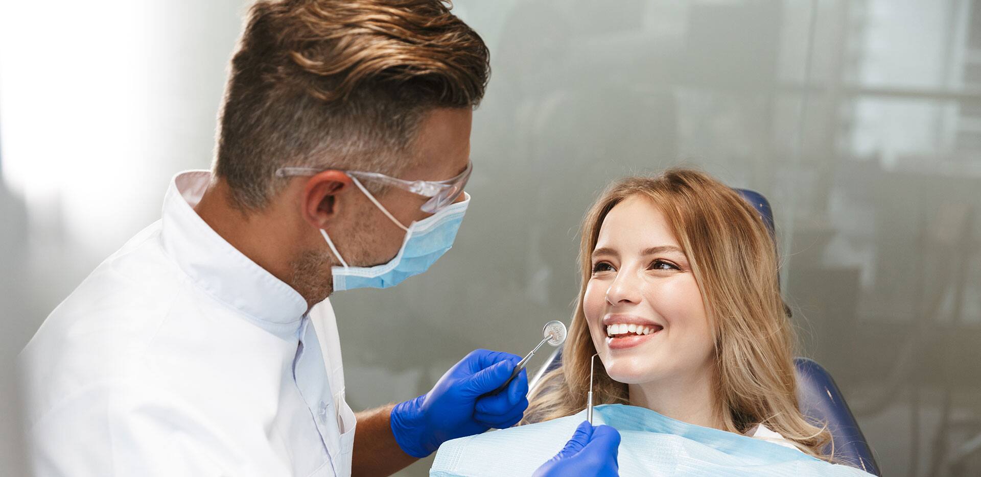 Image of blond woman sitting in dental chair while professional doctor fixing her teeth