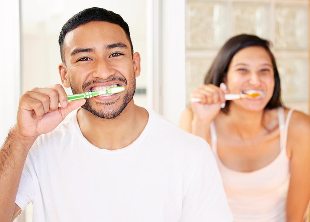 Un homme et une femme se brosse les dents devant un miroir avec le sourire