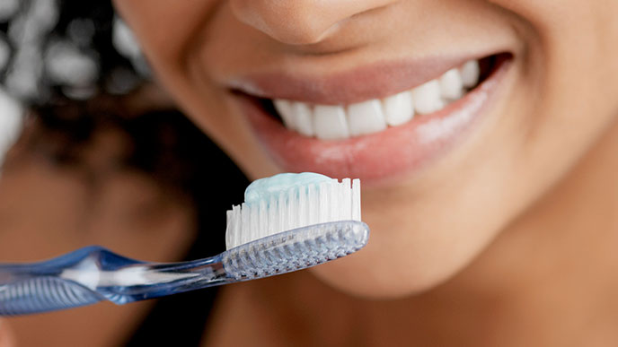gros plan d'une femme souriante qui tient une brosse à dents avec du dentifrice et se brosse les dents.
